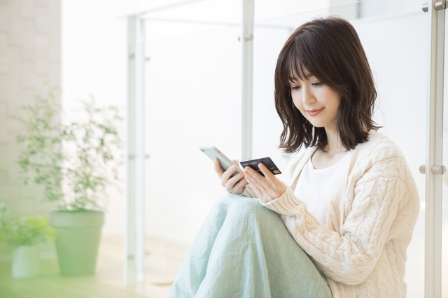クレジットカードを片手にスマホを操作する女性